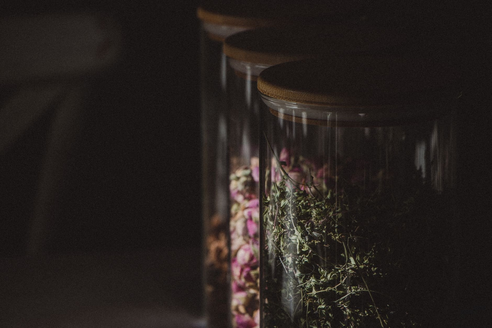 Dark and atmospheric close-up of glass jars filled with spices and herbs in low light.
